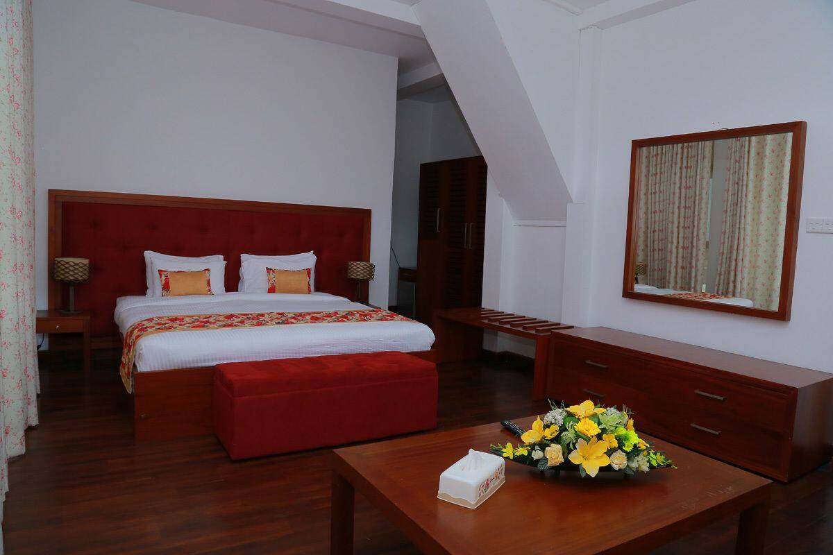 A hotel room with a large bed, a wooden nightstand, a desk with a vase of flowers, and a mirror on the wall.