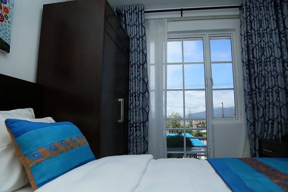 A hotel room with a bed, a window with curtains, and a view of the outside.