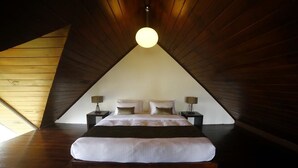 A bedroom with a sloped ceiling, a bed with white bedding, two bedside tables with lamps, and a hanging light fixture. - Blue Meadows - Nuwara Eliya (Nuwara Eliya)