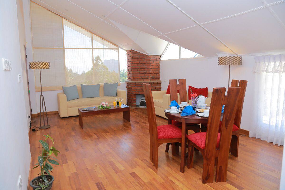 A spacious living area with a wooden dining table, red chairs, a sofa with blue cushions, and a brick fireplace.