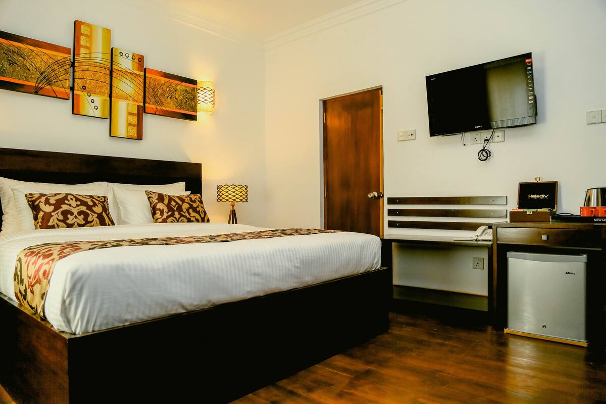 A hotel room with a large bed, a desk with a computer, a television, and a minibar.