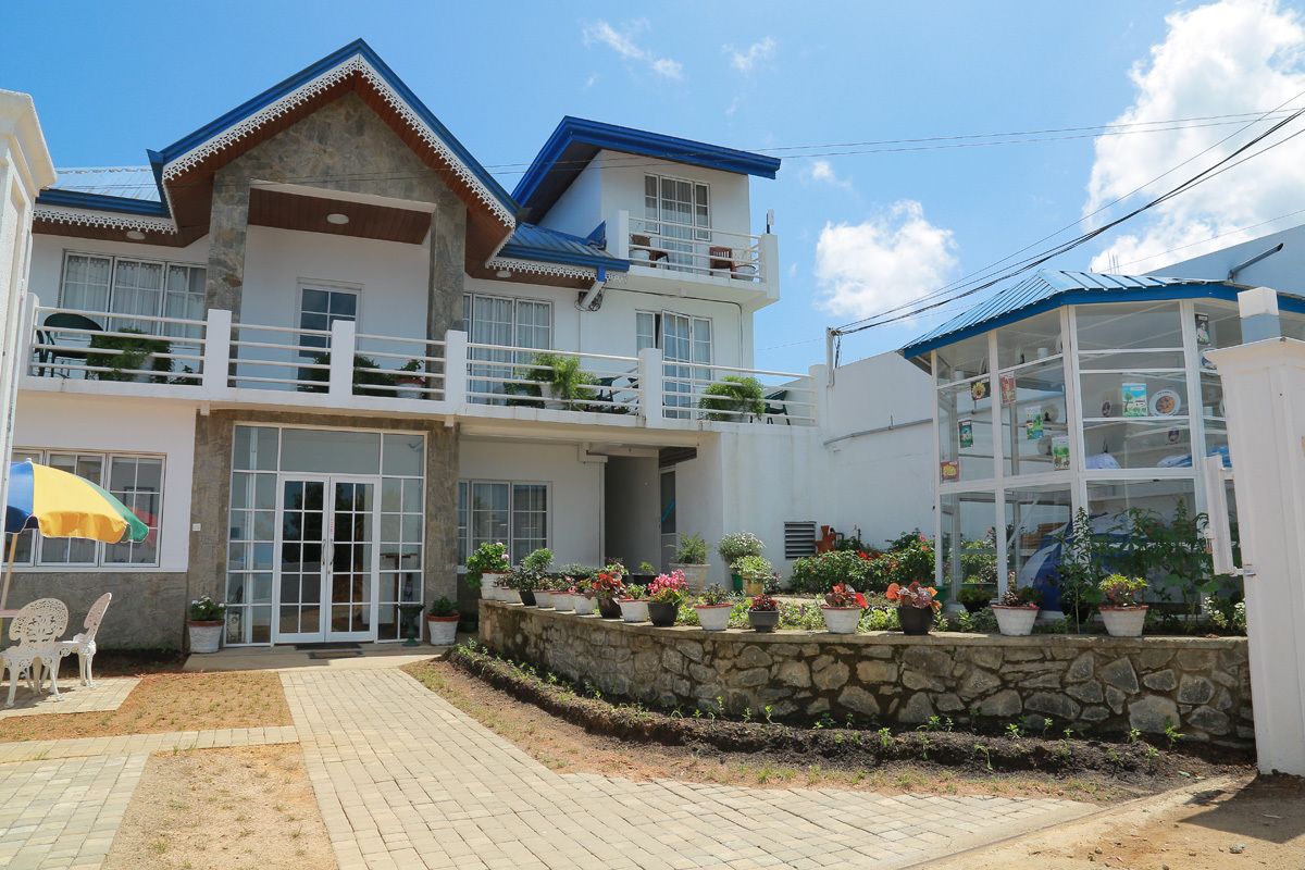 A two-story building with a stone facade, a balcony, and a covered area with potted plants.