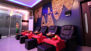 A spa room with massage chairs, red towels, and a statue. - Perfect Hotel (Mandalay)