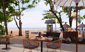 Un espace de restauration en plein air avec des chaises et des tables en osier, une structure à toit de chaume et une vue sur la plage.
