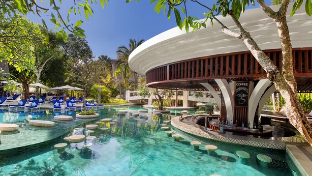 Zona de piscina con agua cristalina, sillones reclinables azules y un área de bar con un cartel que dice 'Coffee Good Idea'.