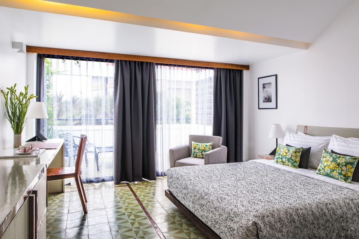 A hotel room with a bed, a chair, a desk, and a window with curtains.