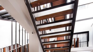 Una escalera moderna con barandillas de madera y peldaños de vidrio, que conduce a un balcón en el segundo piso con vistas de los alrededores.
