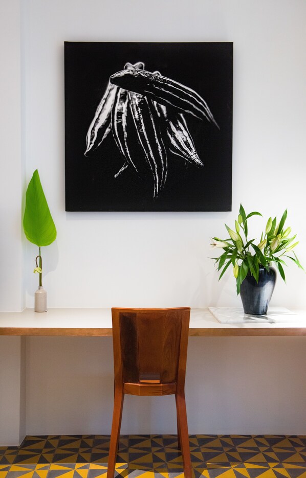 A desk with a chair, a black and white artwork, a green plant, and a potted plant. - 1920 Hotel (Siem Reap)