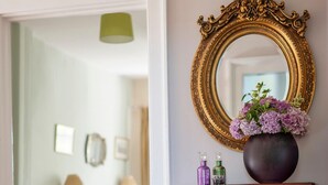 Un couloir avec une console blanche, un grand miroir décoratif et un vase de fleurs.