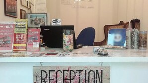 A reception desk with a sign reading "RECEPTION," a computer, a glass vase with flowers, and various informational brochures. - Bed&Breakfast Baznicas 33 (Riga)