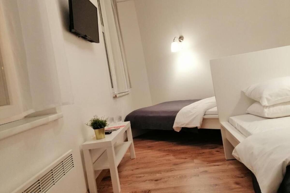 A small, well-lit room with a bed, a bedside table, and a wall-mounted TV.