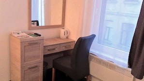 A hotel room with a desk, a chair, a mirror, a window with a view of buildings, and a radiator. - Bed&Breakfast Baznicas 33 (Riga)