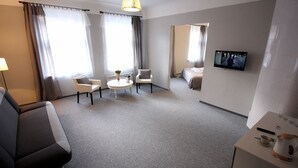 A hotel room with a sofa, two armchairs, a small round table, a TV on the wall, and a bed in the background. - Bed&Breakfast Baznicas 33 (Riga)