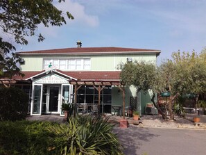 Een receptiegedeelte met een bord voor een hotel en restaurant, zitplaatsen buiten, en een gebouw met een rood dak.