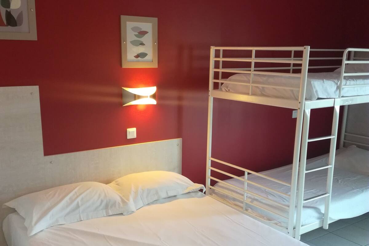 Habitación con literas, una cama individual y una lámpara fijada a la pared.