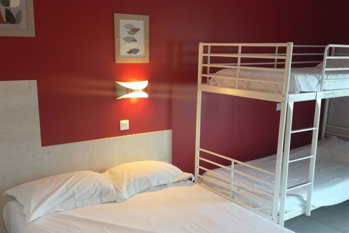Habitación con literas, ropa de cama blanca, una lámpara de pared y un cuadro enmarcado.
