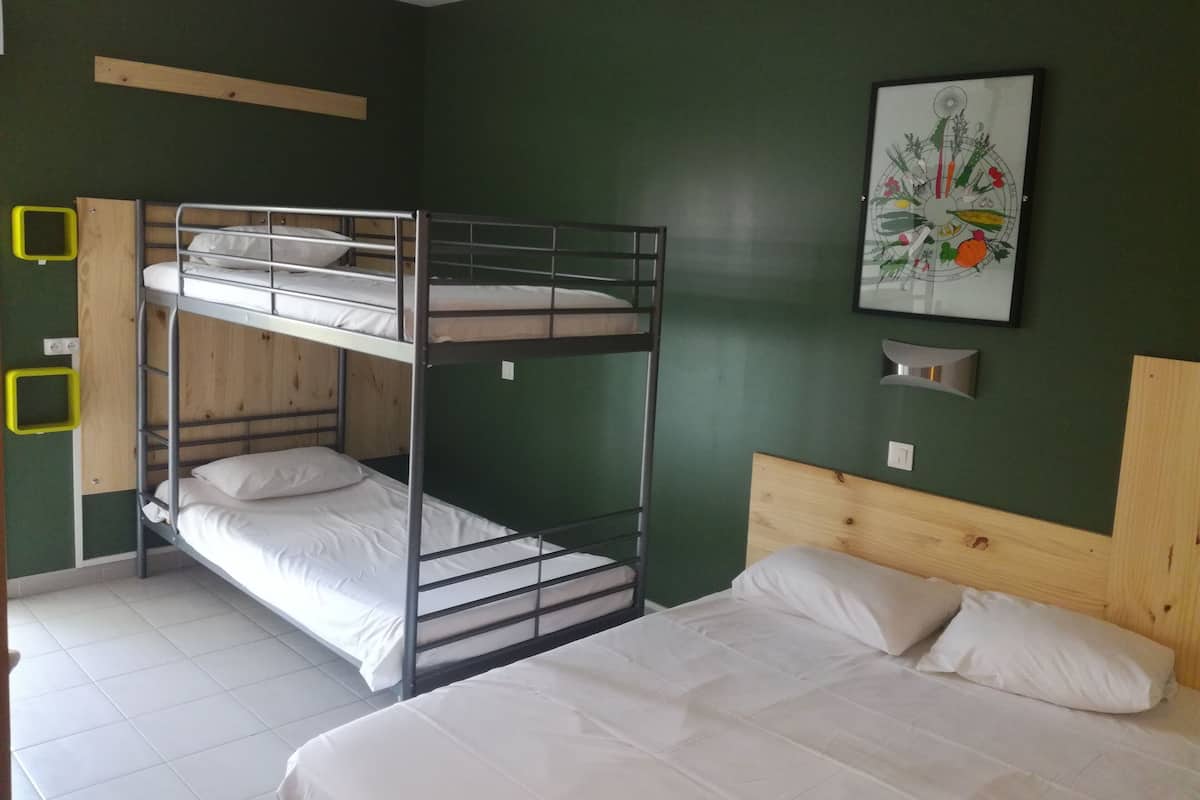 Una habitación con literas y una cama individual, paredes verdes y un cuadro enmarcado.