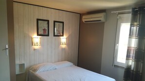 Habitación individual con pared de paneles de madera, dos cuadros enmarcados, un equipo de aire acondicionado y una ventana con cortinas.