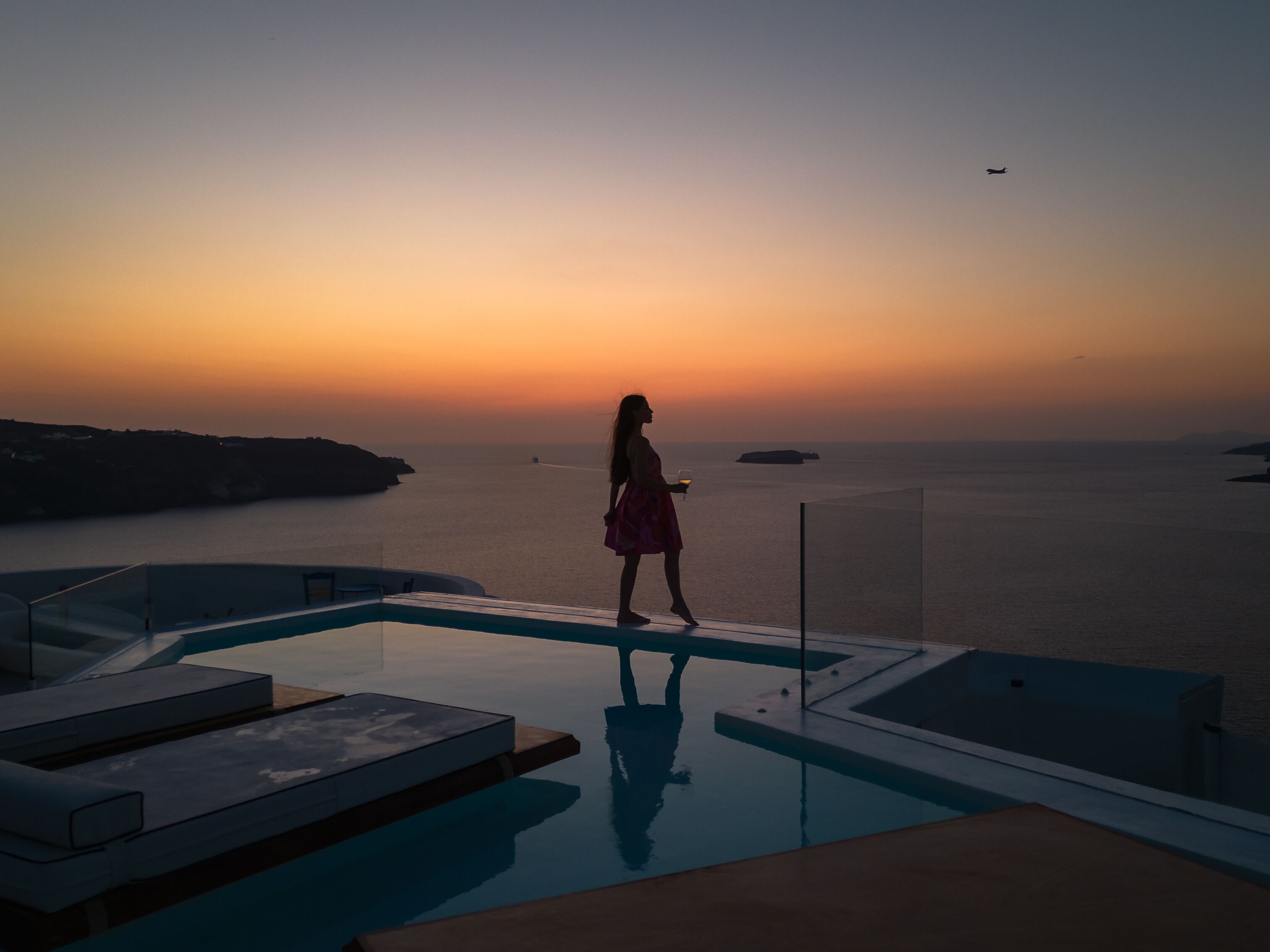 Eine Person steht am Pool mit Blick auf das Meer und den Sonnenuntergang.