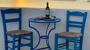 Un balcón con dos sillas azules, una mesa, una botella de vino y una copa.
