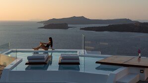 Una piscina infinita con una persona sentada, con vistas a la costa y a islas distantes.