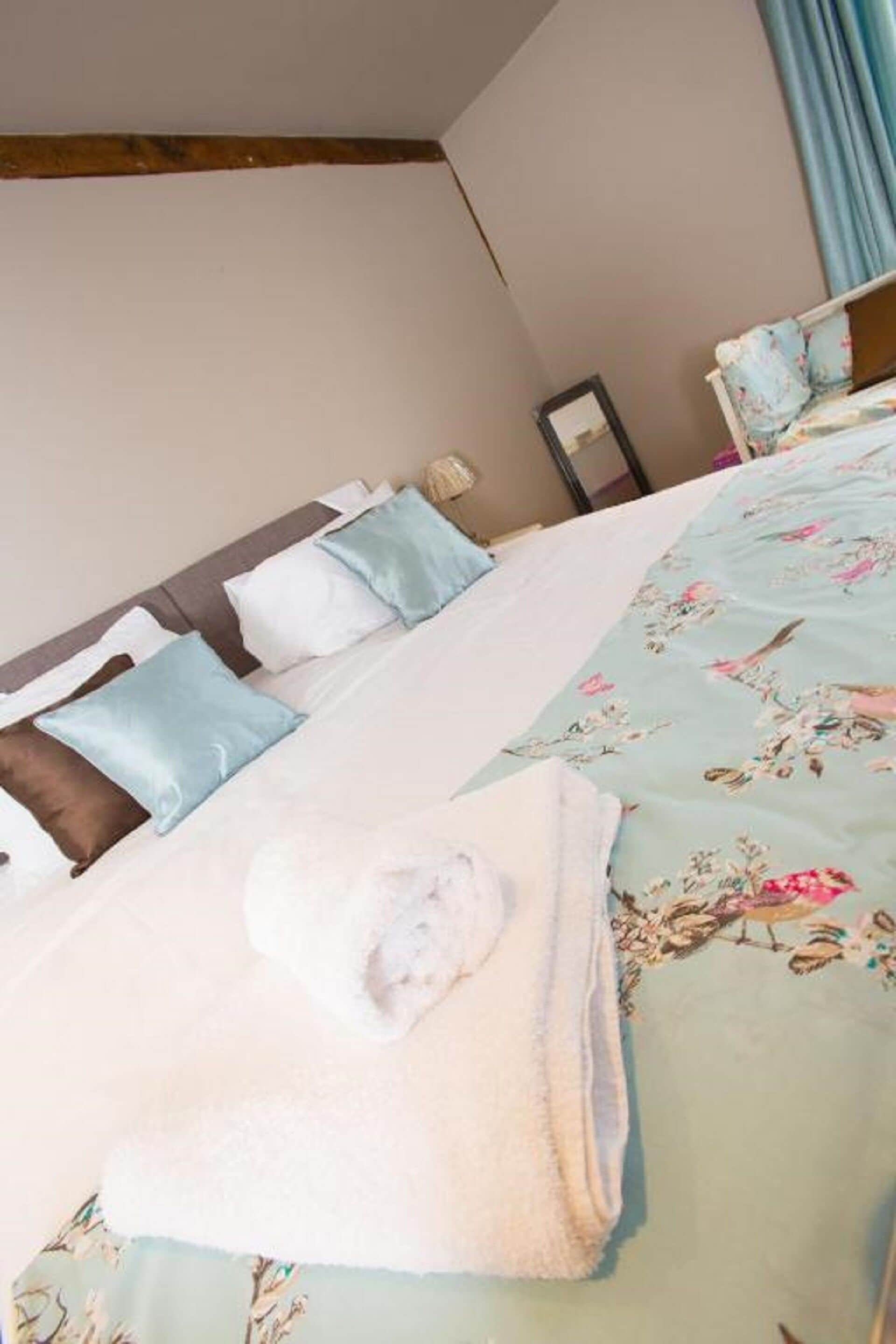 A neatly made bed with a floral duvet, pillows, and a folded towel.