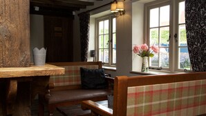 A cozy room with a wooden bench, a table, and a window with curtains. - The Harvard Inn (Ingatestone)