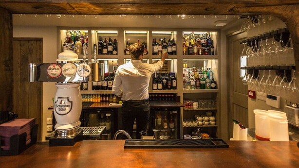 A bar with a bartender preparing drinks, shelves of liquor bottles, and a beer tap. - The Harvard Inn (Ingatestone)