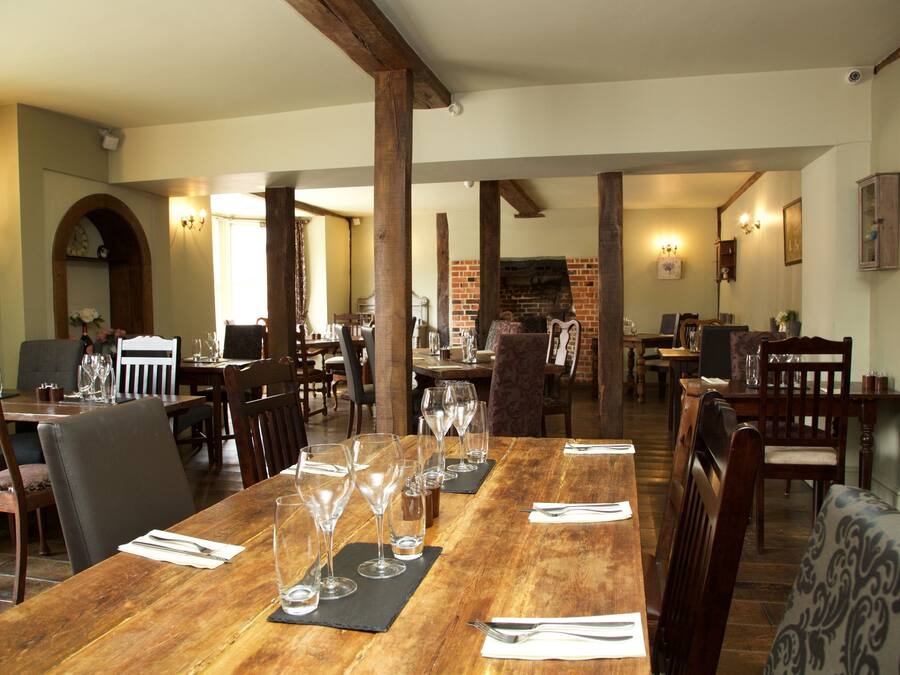Un espace repas avec des tables et des chaises en bois, une cheminée en briques et un lustre.
