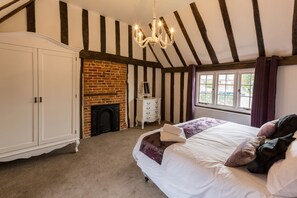 A bedroom with a large bed, a white wardrobe, a fireplace, and a window with curtains.