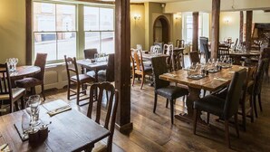 A restaurant with wooden tables and chairs, large windows, and a brick wall. - The Harvard Inn (Ingatestone)