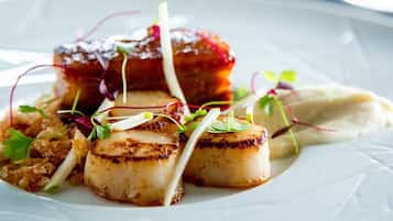 Un plato de vieiras a la plancha, adornado con microgreens y verduras en rodajas finas.