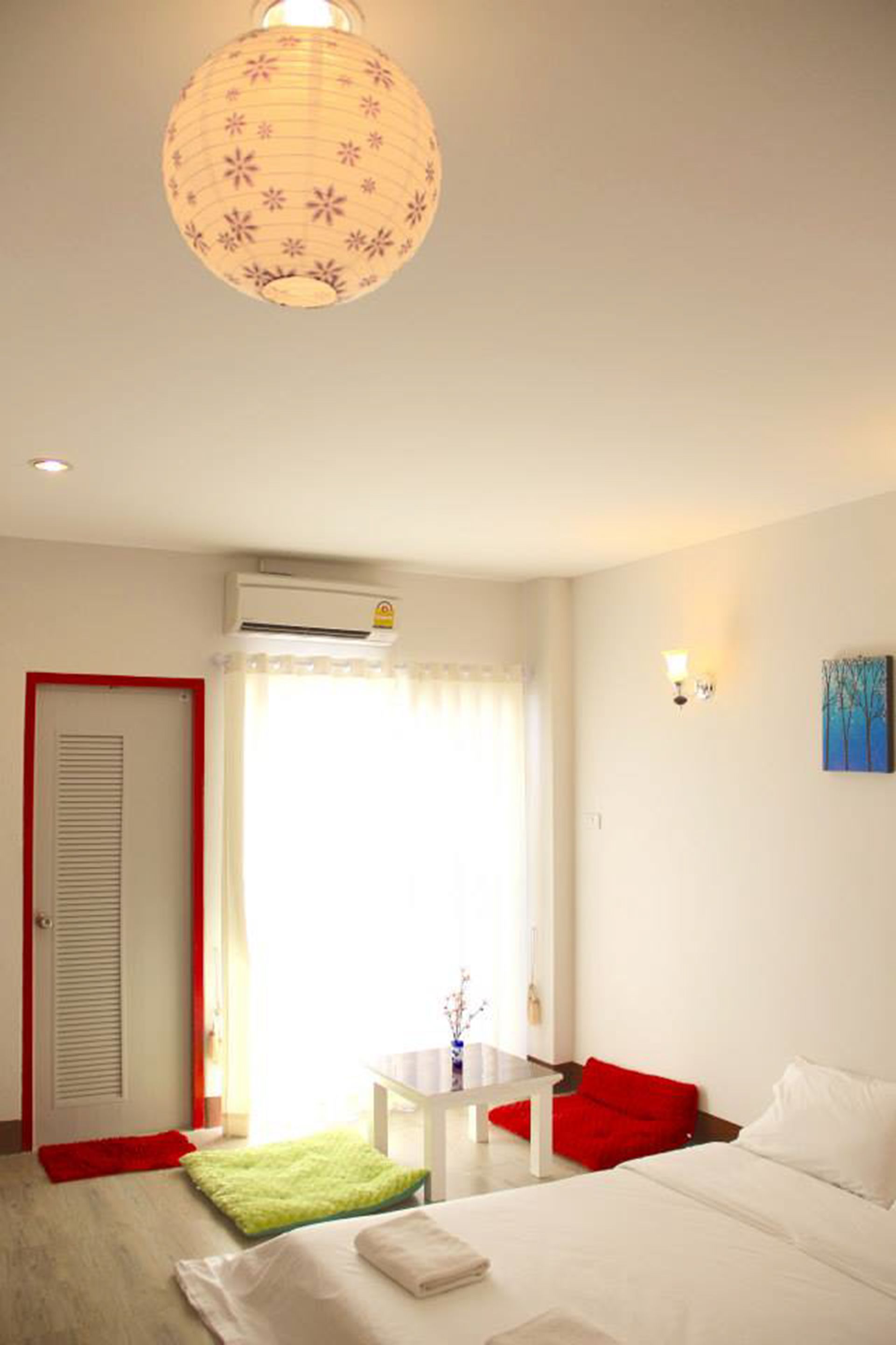 A hotel room with a bed, a small table, a red chair, a green rug, and a ceiling light.