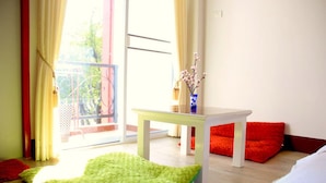 Una habitación con alfombra verde y mullida, una mesa blanca con un florero y cojines rojos.