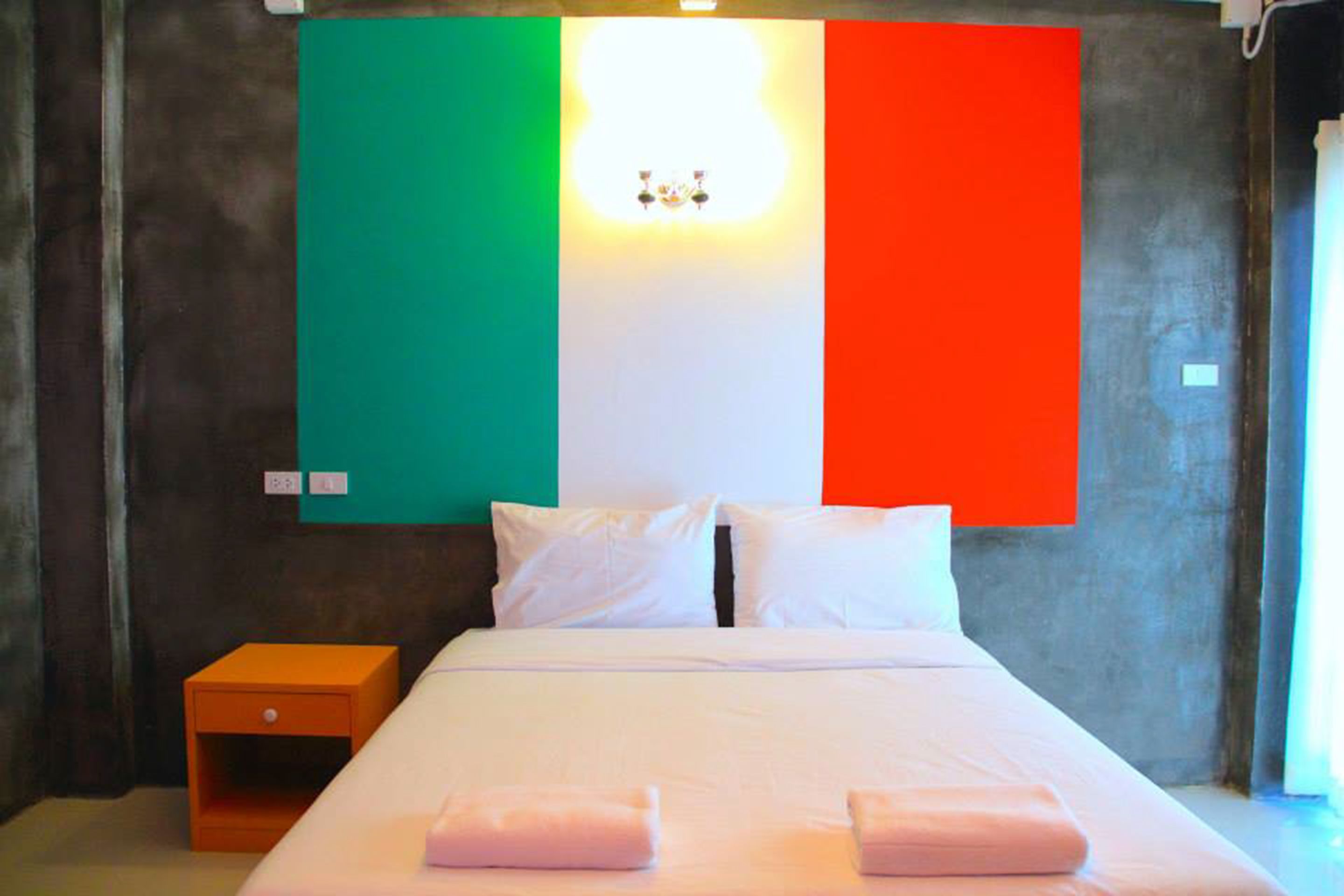 A hotel room with a bed, pillows, a nightstand, and a wall with a flag design.