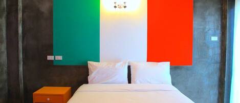 A hotel room with a bed, pillows, a nightstand, and a wall with a flag design.