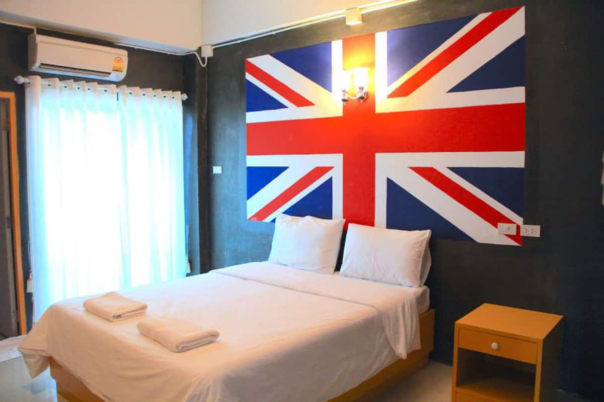 A hotel room with a large bed, white bedding, a small wooden nightstand, and a wall with a Union Jack flag.