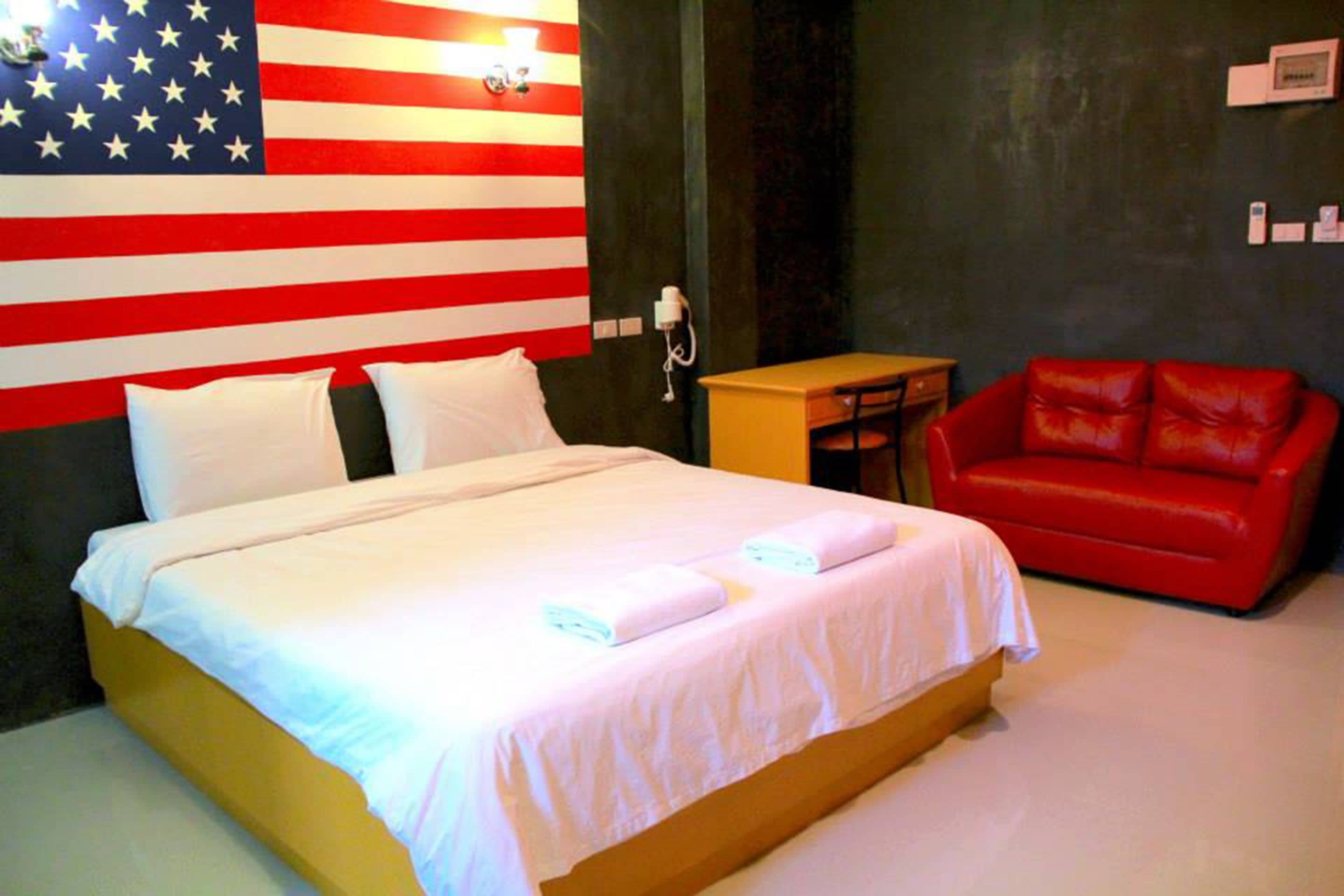 A hotel room with a bed, a red leather couch, a small table, and a wall with an American flag design.