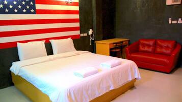A hotel room with a bed, a red leather couch, a small table, and a wall with an American flag design.