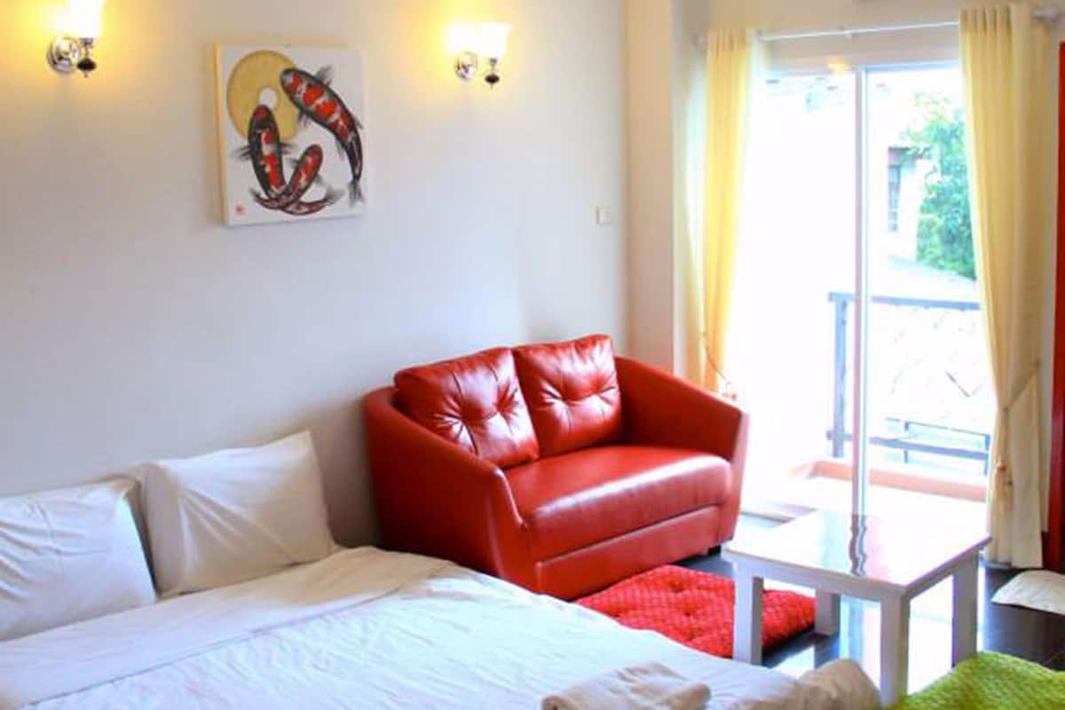 A hotel room with a large bed, a red leather sofa, a small table, and a painting on the wall.
