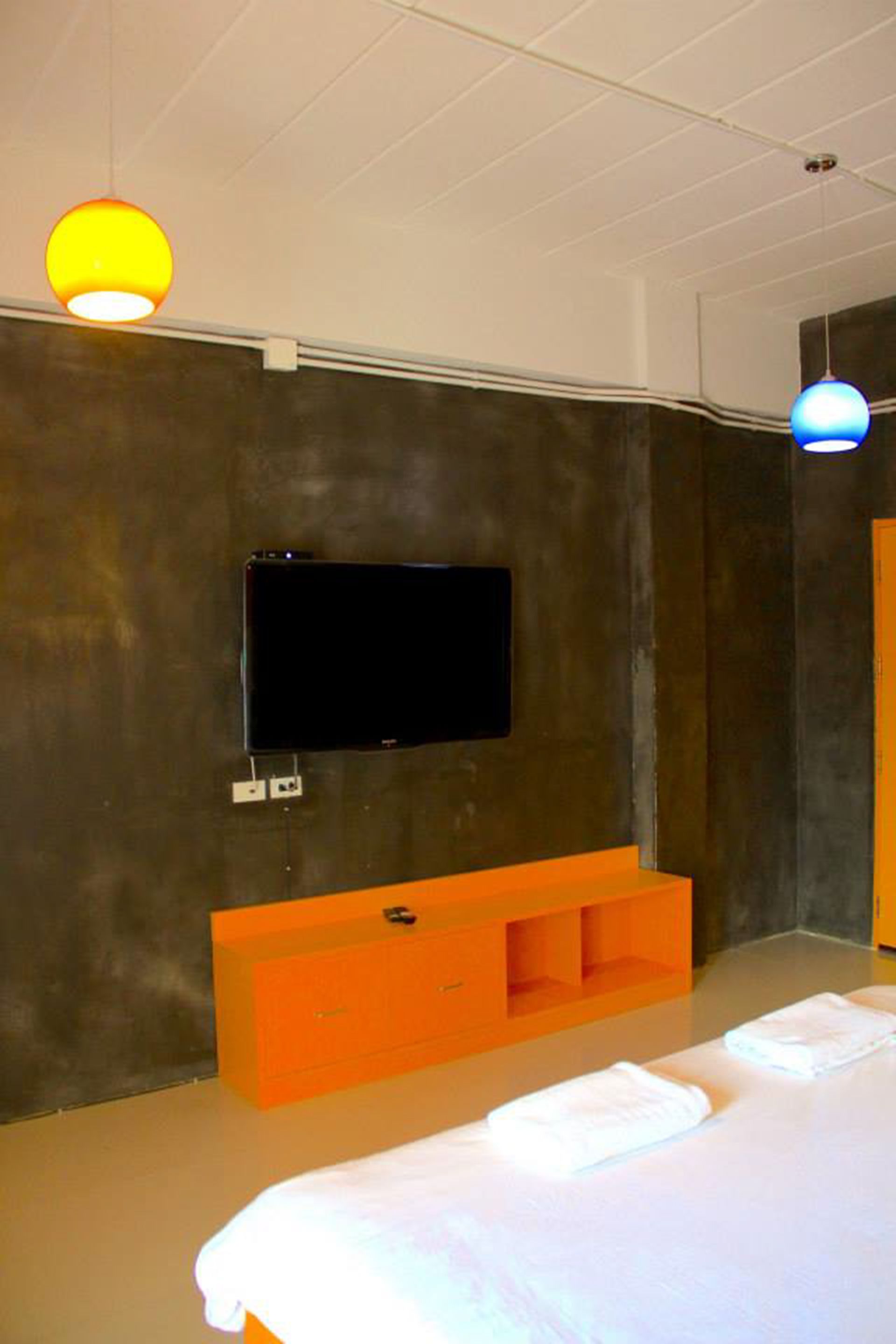 Et moderne hotelværelse med en stor seng, et fladskærms-tv monteret på væggen, et orange konsolbord og to hængende lamper.