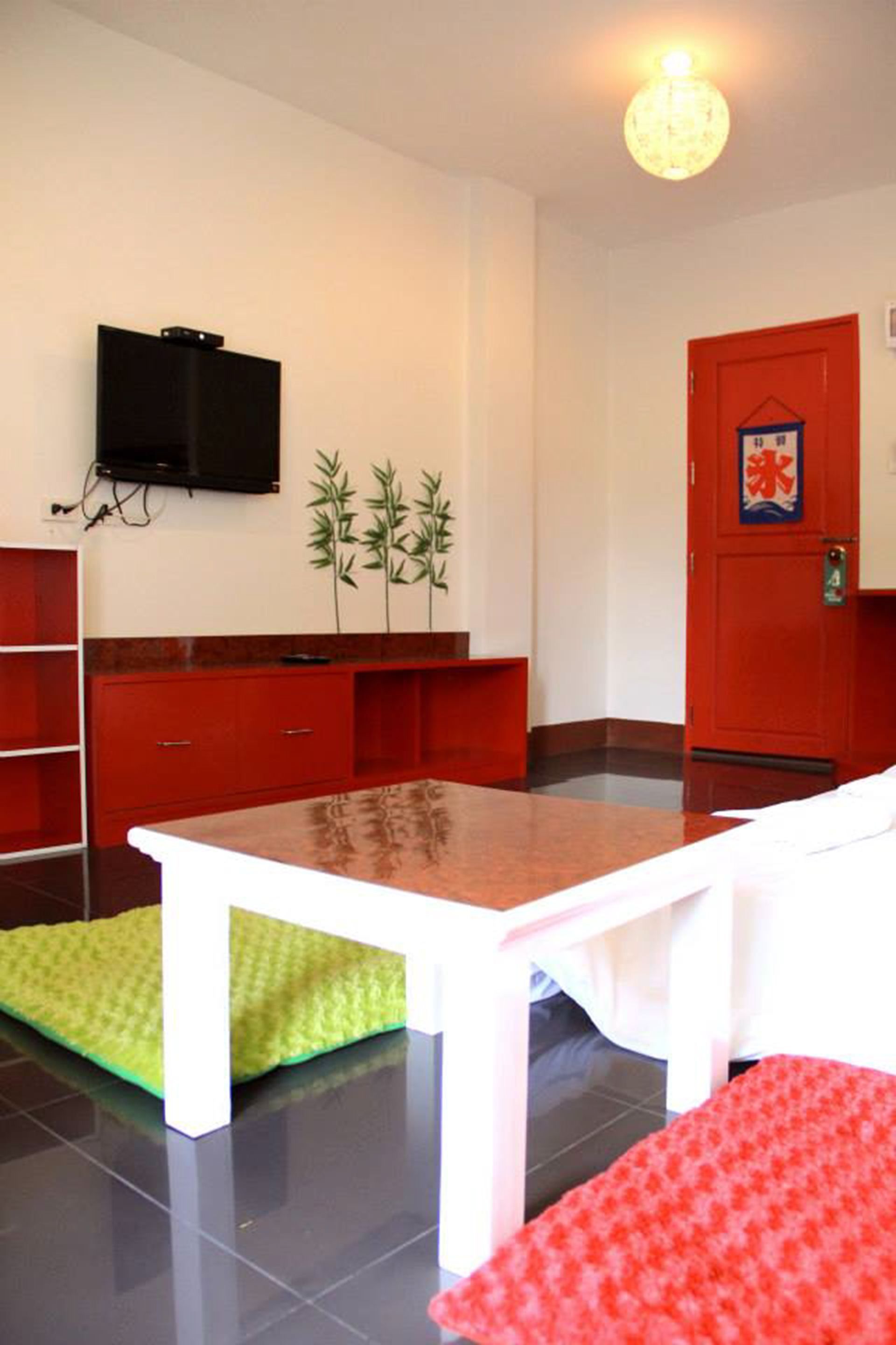 A room with a white table, red cabinets, a red door, a television on the wall, and a small plant.