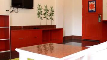 A room with a white table, red cabinets, a red door, a television on the wall, and a small plant.