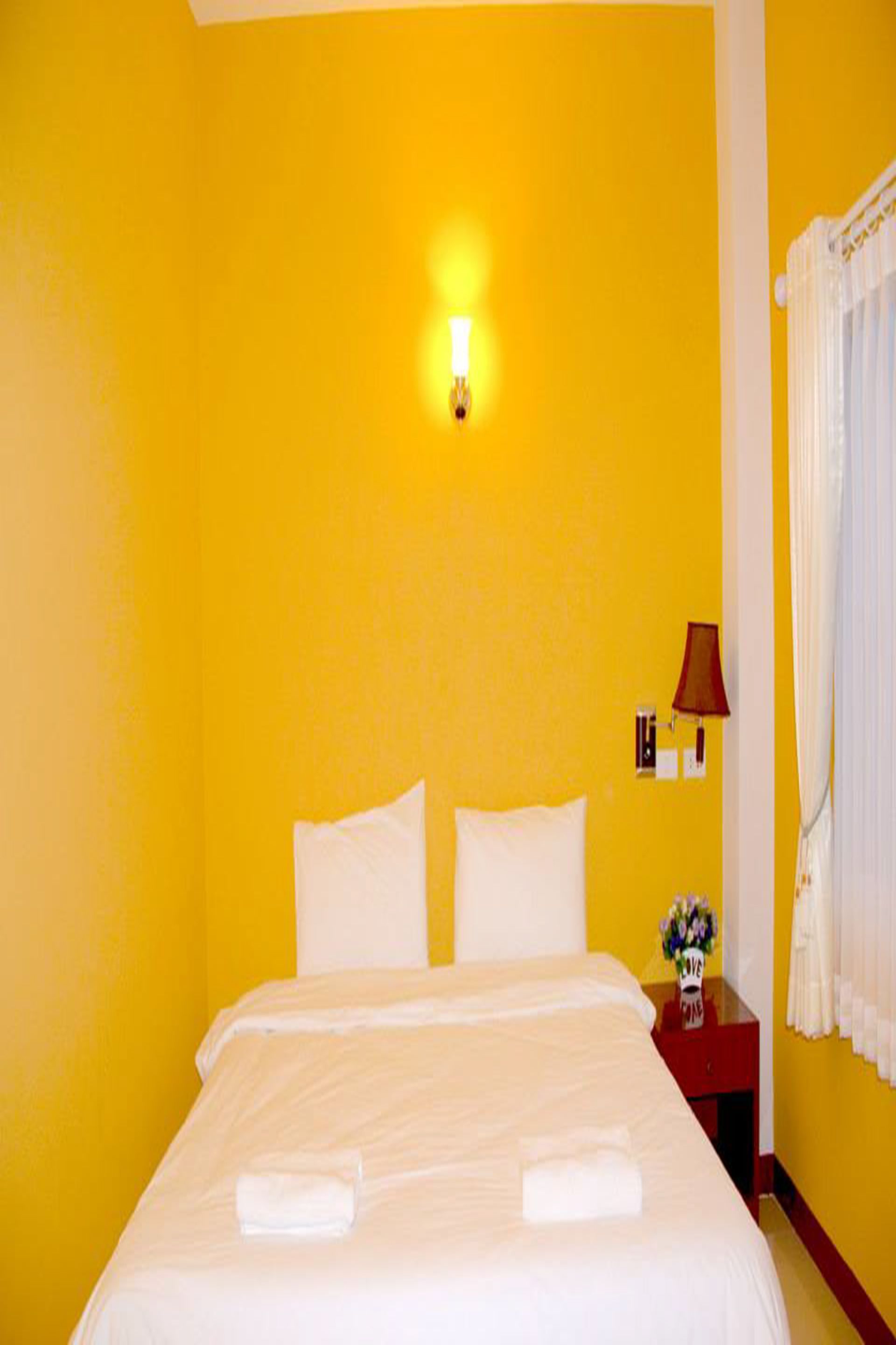 Een hotelkamer met een bed, een nachtkastje met een lamp en een raam met gordijnen.