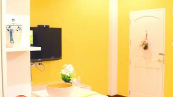 A bright yellow room with a white counter, a television mounted on the wall, and a door with a flower wreath.