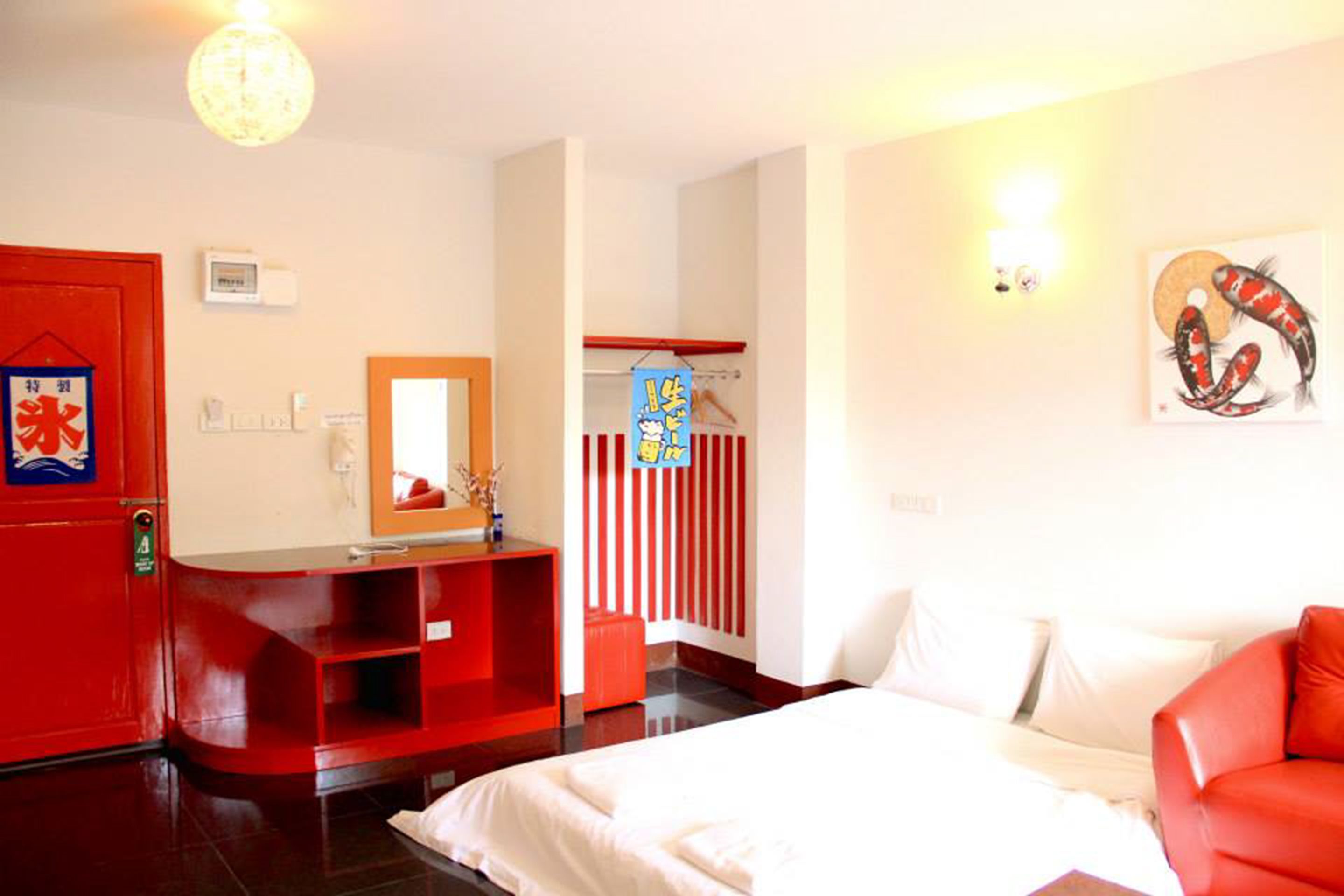 Une chambre d’hôtel avec un lit, une armoire rouge, un miroir, une cloison à rayures rouges et blanches, et une œuvre d’art accrochée au mur.
