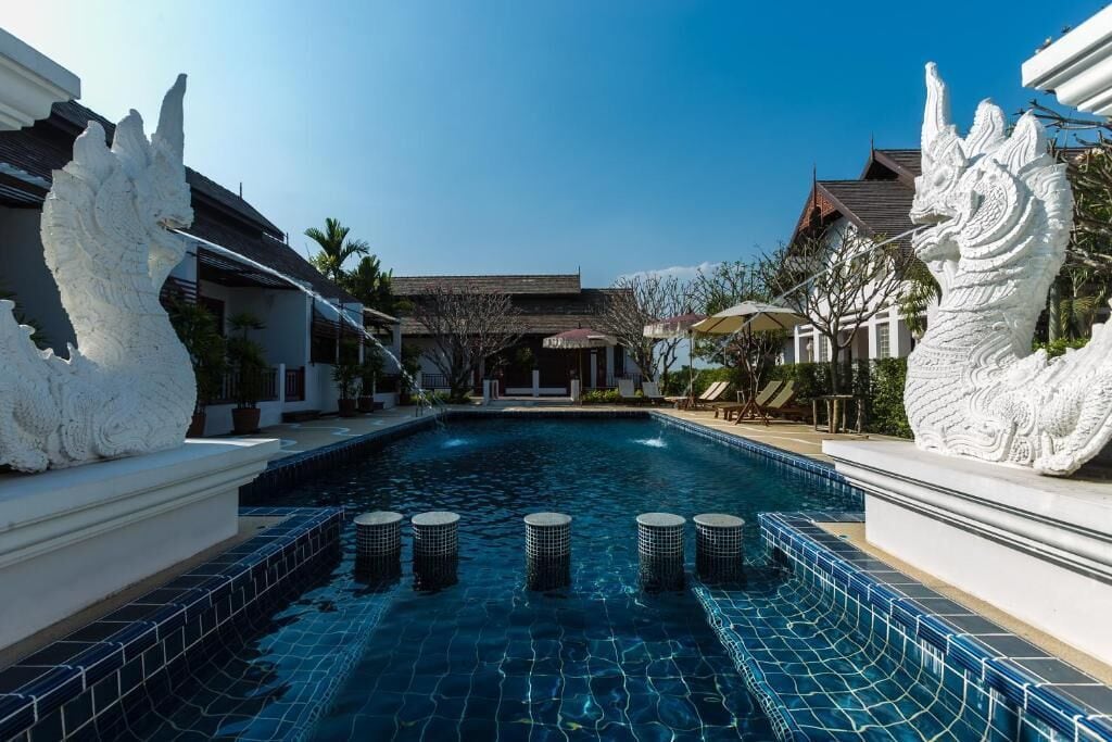 A swimming pool with decorative white statues on either side, surrounded by buildings with traditional architecture.
