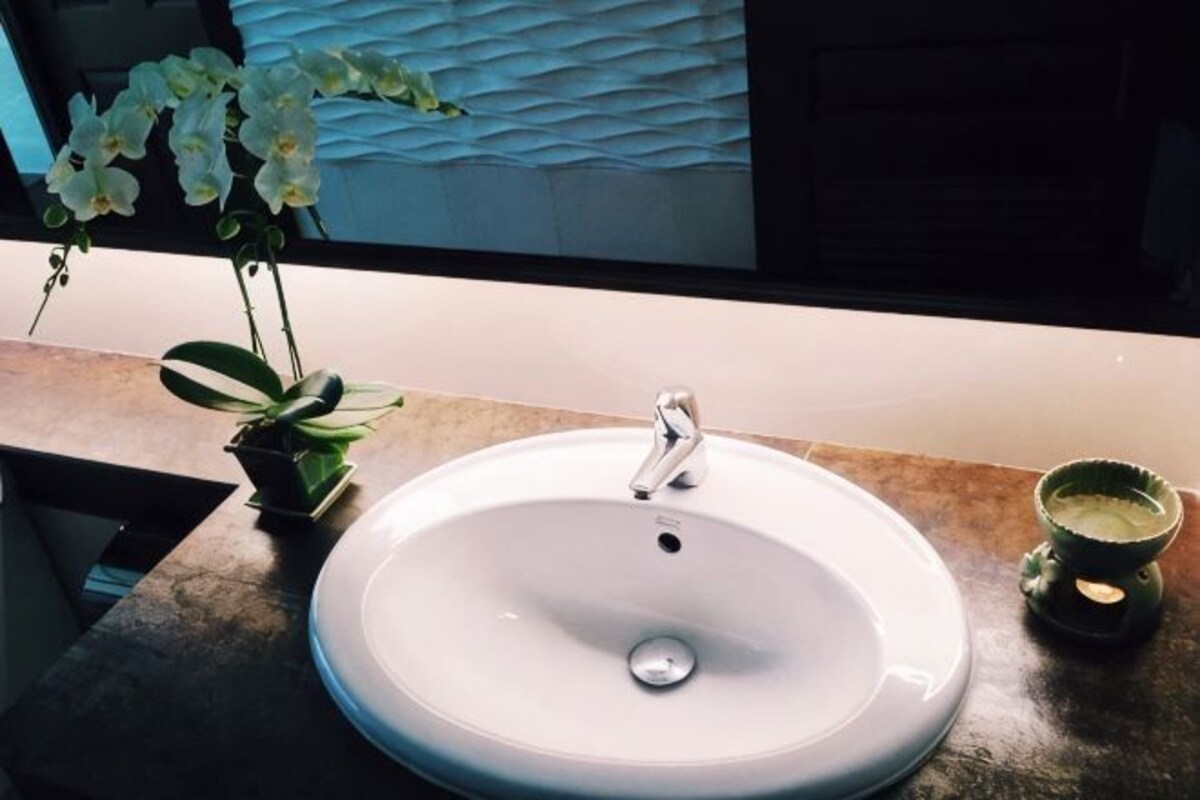 Un lavamanos de baño con un grifo moderno, una orquídea en maceta y un pequeño recipiente verde.