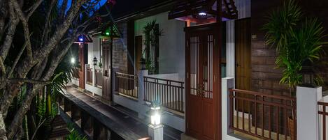 A traditional wooden house with a balcony, a wooden door, and a small garden area.