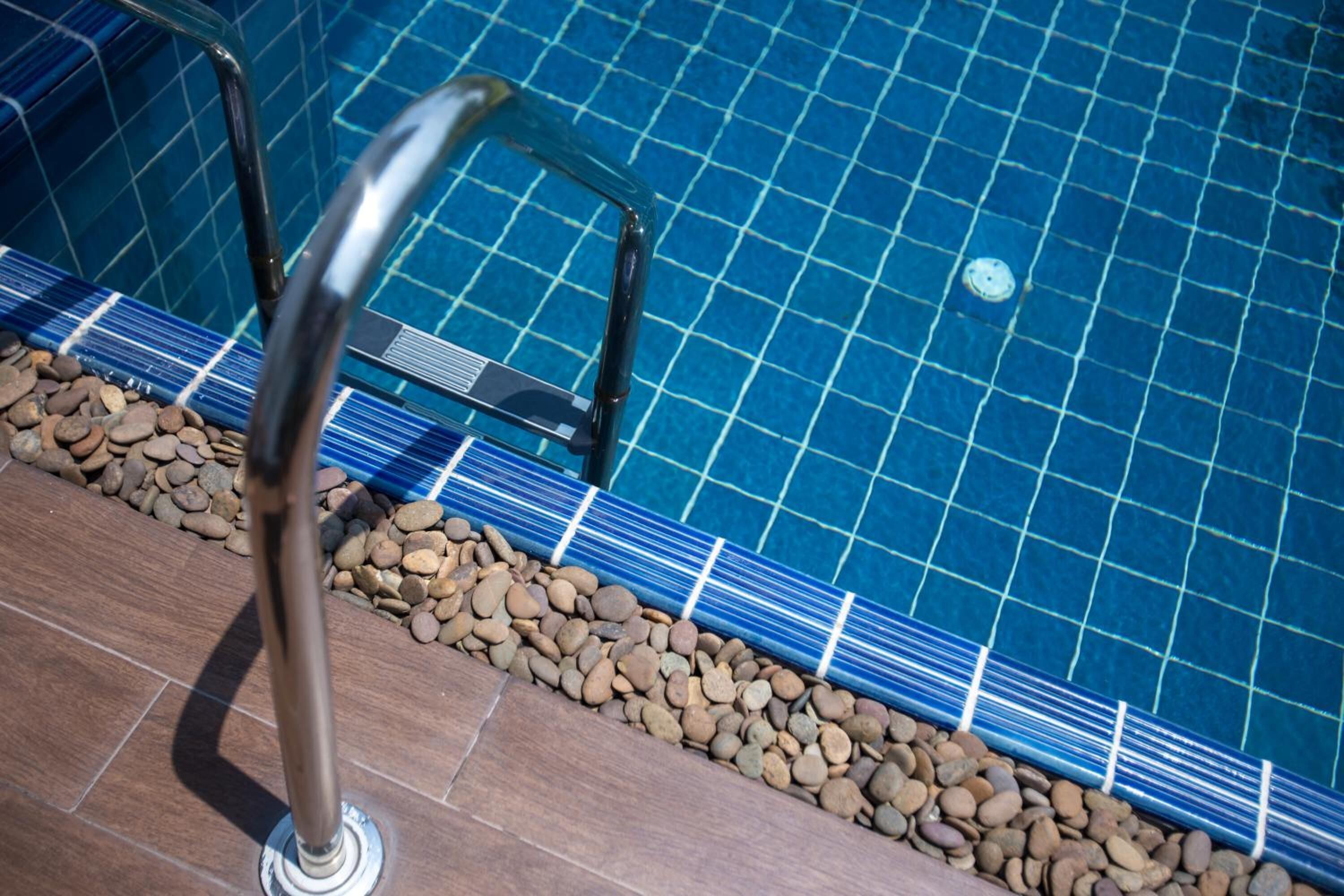 A pool with a tiled edge, metal handrails, and a pebble border.